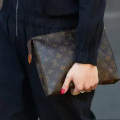 Dłoń trzyma brązową kopertówkę Louis Vuitton z monogramem.