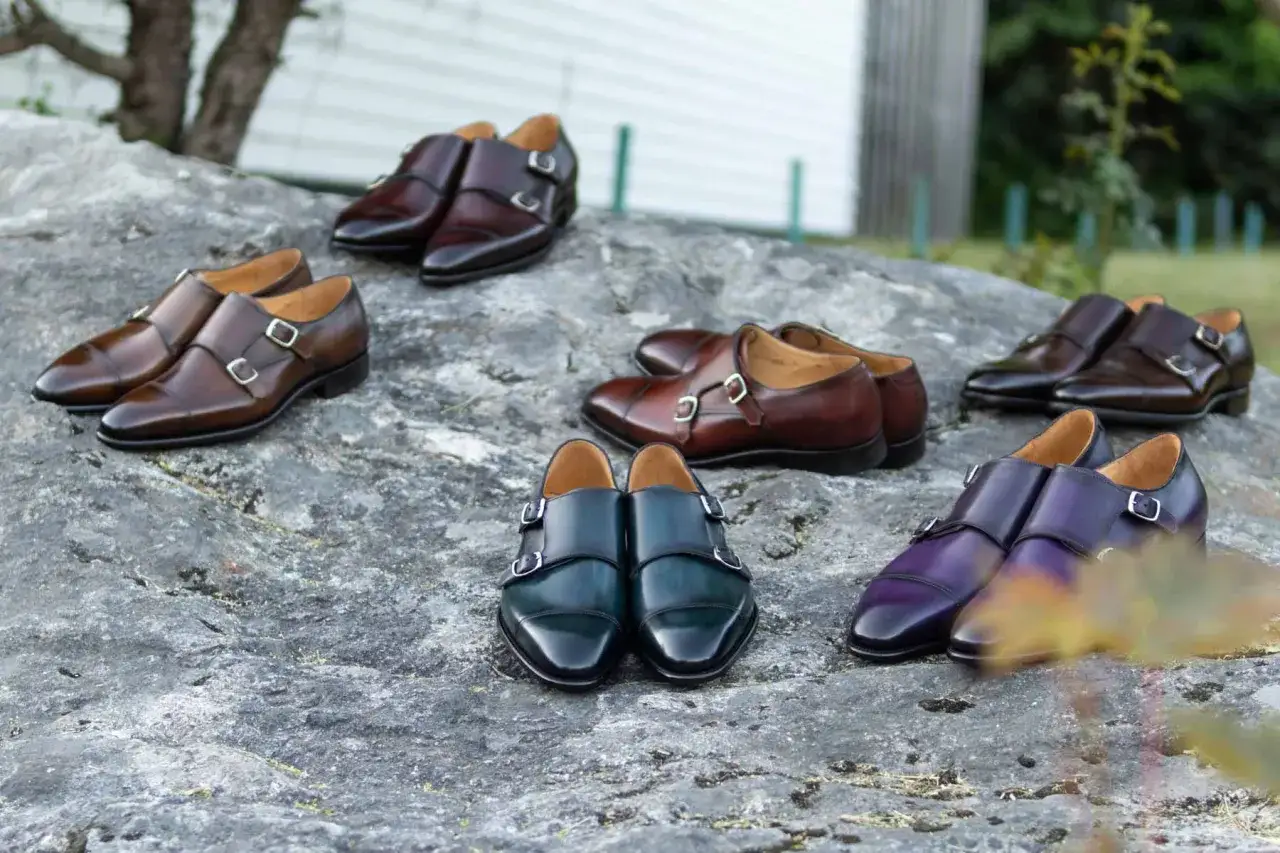 Eleganckie, skórzane buty męskie z podwójnymi klamrami. Luksusowe marki butów męskich prezentują swoje wyroby w różnych odcieniach brązu, zieleni i fioletu.
