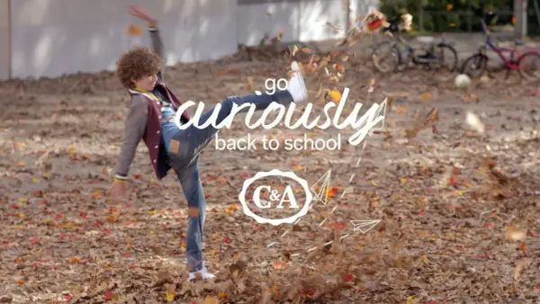 Chłopiec w jesiennych ubraniach kopie liście, z napisem "go curiously back to school" i logo C&A.